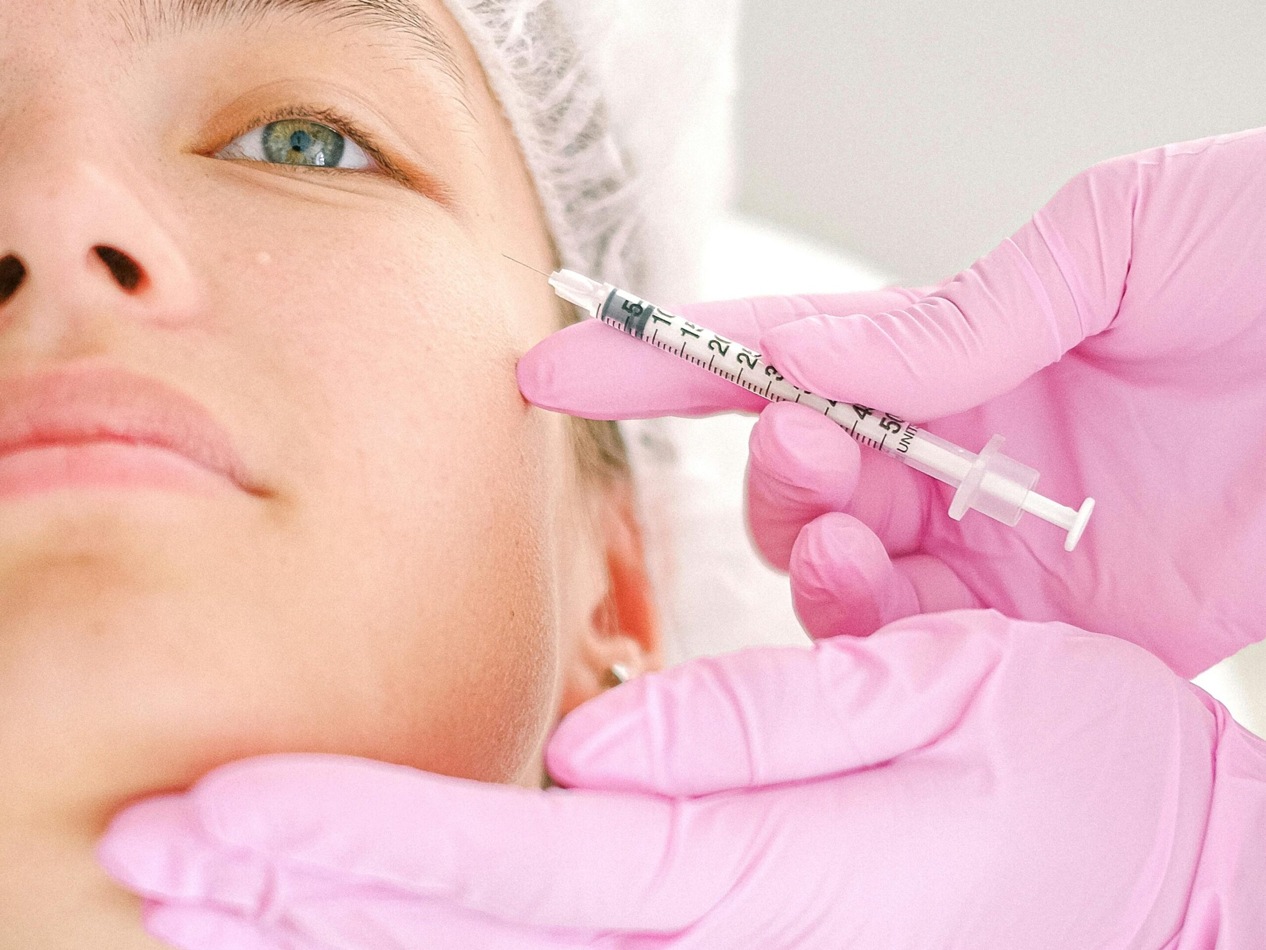 Close-up of a beautician administering facial injection treatment to a woman in a clinical setting.
